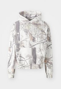 Sweatshirt com capuz num padrão de camuflagem, apresentando ramos e folhas em cinza, branco e tons terrosos suaves. Inclui um bolso frontal.