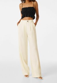 Zwarte geplooide crop top met ruffled rand, gecombineerd met hoogwater, wijde crèmekleurige broeken met een knoopdetail in de taille.