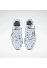 Zapatillas deportivas blancas con una parte superior sintética lisa, correa ajustable, cordones, detalles perforados y suelas de goma.