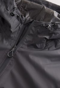 Veste imperméable noire avec fermeture éclair à l’avant et capuche ajustable avec cordon et bloque-cordons.