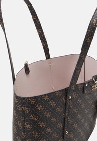 Sac fourre-tout noir avec motif de logo doré, finition en cuir lisse, doublure intérieure rose clair et accents en matériel doré. Forme structurée.