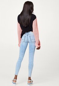 Neulottu musta ja vaaleanpunainen pusero, jossa pitkät hihat, yhdistetty vaaleansinisiin kapealahkeisiin farkkuihin ja hopeisiin sandaaleihin, nähtynä takaa.