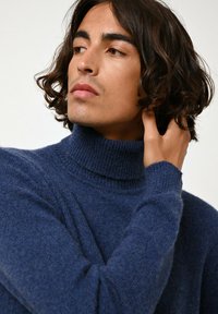 Pull en col roulé bleu marine en maille douce, avec des poignets et un col côtelés, offrant une coupe décontractée et des détails en texture.