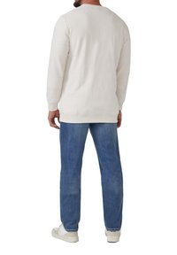 Sweatshirt beige clair à manches longues avec un col rond et des poignets côtelés, associé à un jean bleu clair et des baskets blanches. Design simple et épuré.