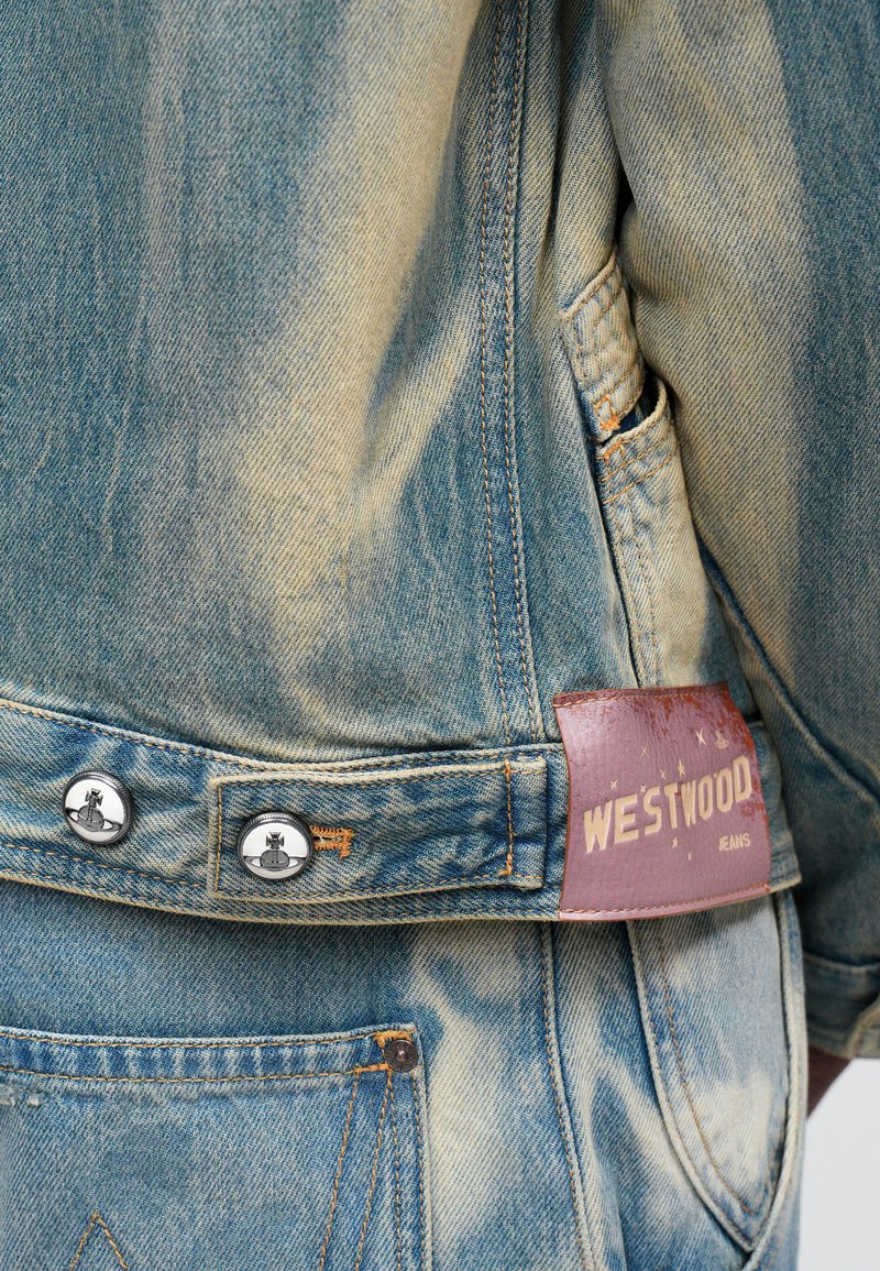 Giubbotto di jeans blu chiaro con texture sbiadita, bottoni argentati e un'etichetta in pelle marrone con la scritta "WESTWOOD JEANS" sul retro.