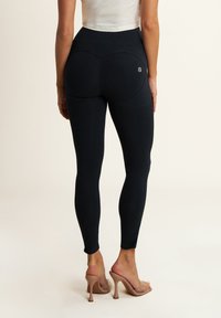 Leggings neri con vita alta, texture liscia e dettagli con cuciture sul retro. Abbinati a sandali con tacco trasparente per un contrasto.