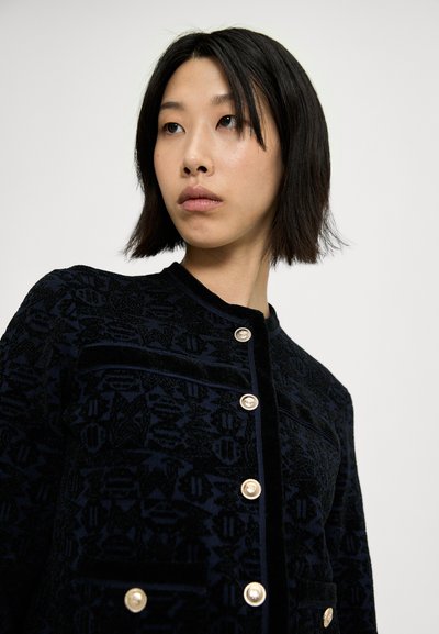 Chaqueta de patrón navy hecha de tejido texturizado, con botones dorados, un cuello redondo y un diseño ajustado con bolsillos frontales.