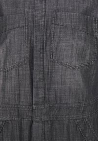 Mono de mezclilla gris oscuro con acabado texturizado, dos bolsillos en el pecho y cintura ajustada para un look estructurado.