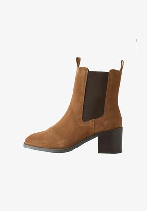 Brun ruskindsankelstøvle med elastiske sidestykker, en spids tå og en kraftig træhæl. Har træk-flapper for nem påtagning.