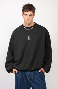 Zwarte oversized sweatshirt met verlaagde schouders, met een minimalistisch wit karakterontwerp op de borst. Draagt het met losse blauwe jeans.