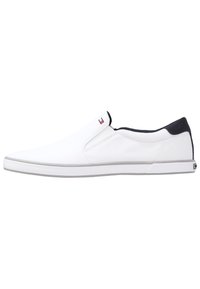 Scarpe slip-on bianche in tela con un accentuazione navy sul tallone, suola in gomma testurizzata e un piccolo tag con il logo sul lato.