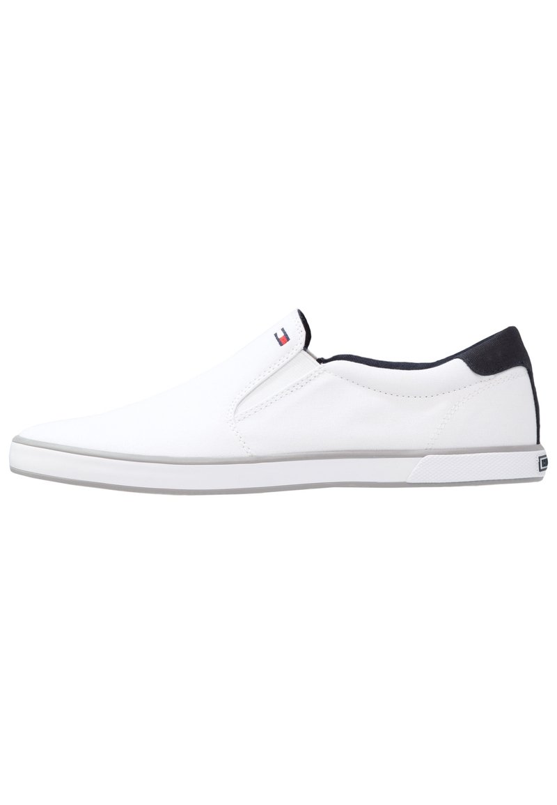 Scarpe slip-on bianche in tela con un accentuazione navy sul tallone, suola in gomma testurizzata e un piccolo tag con il logo sul lato.