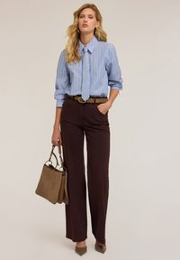 Ein blau-weiß gestreiftes Hemd mit Kragen und Krawatte, kombiniert mit braunen weiten Hosen und einer beigen Wildleder-Handtasche. Braune Absätze runden das Outfit ab.