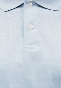 Ανοιχτόγαλάζιο πόλο μπλουζάκι με δύο λευκά κουμπιά και επίπεδη γιακά, που δείχνει υφή από λεπτό πλεκτό ύφασμα.