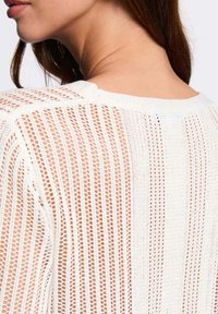 Top bianco lavorato a maglia con design a rete aperta, caratterizzato da righe verticali e scollatura arrotondata, che mette in mostra un tessuto testurizzato.