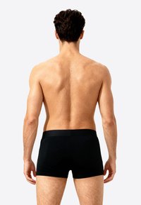 Zwarte boxer briefs met een gladde textuur en een brede tailleband, gezien van achteren op een mannelijk figuur tegen een lichte achtergrond.