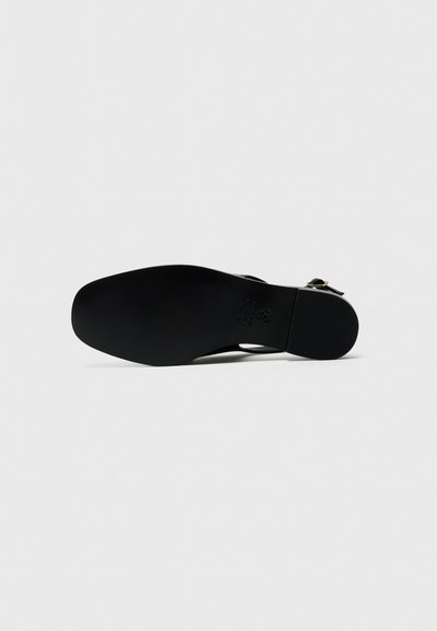 Suola di scarpa nera con una texture liscia, punta arrotondata e tacco leggero. Presenta un design ritagliato e cinturini regolabili con dettagli in metallo.