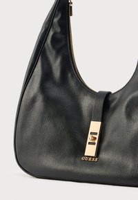 Czarna skórzana torba na ramię o teksturowanym wykończeniu, z zamkiem błyskawicznym w złotym kolorze i prostokątnym metalowym elementem z logo "GUESS".
