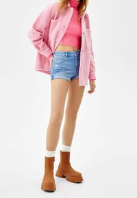 Rosa ullblandad oversized jacka över en rosa ribbad polotröja, kombinerad med denimshorts och bruna plattformankelstövlar med ribbade muddar.