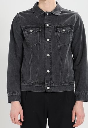 Veste en denim noire à manches longues, fermeture boutonnée à l'avant, deux poches poitrine à rabat avec boutons, portée par une personne en position neutre.