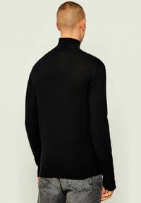 Maglione nero a collo alto con un design aderente, texture liscia e maniche lunghe, abbinato a jeans di denim grigi. Orlo sventolante e colletto a costine.