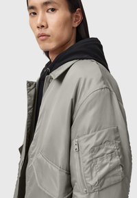 Chaqueta bomber de gran tamaño en gris claro, fabricada con un material suave y acolchado, con un bolsillo con cremallera, puños acanalados y un cuello puntiagudo.