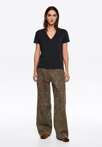 Czarny t-shirt z dekoltem w serek z małymi białymi kropkami, zestawiony z szerokimi brązowymi spodniami o fakturze i geometrycznym wzorze.