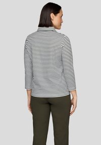 Langärmeliges, gestreiftes Oberteil in Schwarz und Weiß mit Kragen und Seitenschlitzen, kombiniert mit dunkelgrünen Hosen.