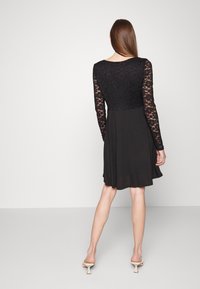 Vestido preto com corpete de rendas e mangas longas, com cintura justa e saia ampla. Textura suave com um design clássico.