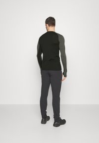 Czarna koszula z długim rękawem z szarymi teksturowanymi ramionami, zestawiona z ciemnymi spodniami i czarnymi butami. Gładkie tło podkreśla uwagę na stroju.