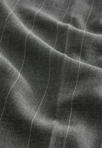 Texturiert grauer Stoff mit dünnen vertikalen Streifen in einem helleren Farbton. Das Material wirkt weich mit dezenten Falten und einer glatten Oberfläche.