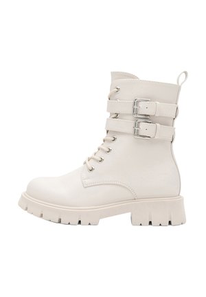 Stivaletto alla caviglia color avorio con suola robusta, chiusura frontale con lacci e due cinturini regolabili con fibbia intorno alla parte superiore della caviglia.