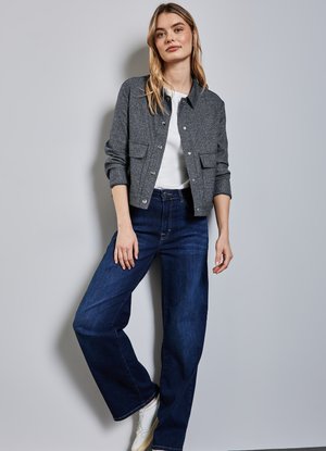 Veste grise courte avec deux poches avant, associée à un t-shirt blanc et un jean large bleu foncé. Des baskets blanches complètent la tenue.
