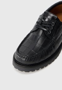 Black leather shoe with a crocodile texture, round toe, and sturdy rubber sole. Features decorative stitching and lace-up closure.