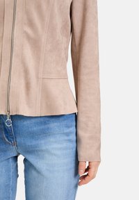 Ljusrosa mockajacka med en figurnära design, dragkedja och långa ärmar, kombinerad med blå denimjeans.