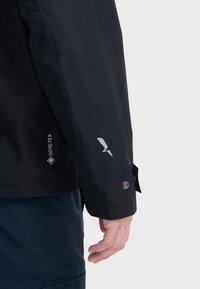 Manche de veste en GORE-TEX noir au design épuré, avec un logo réfléchissant, une fermeture à bouton et une texture lisse.