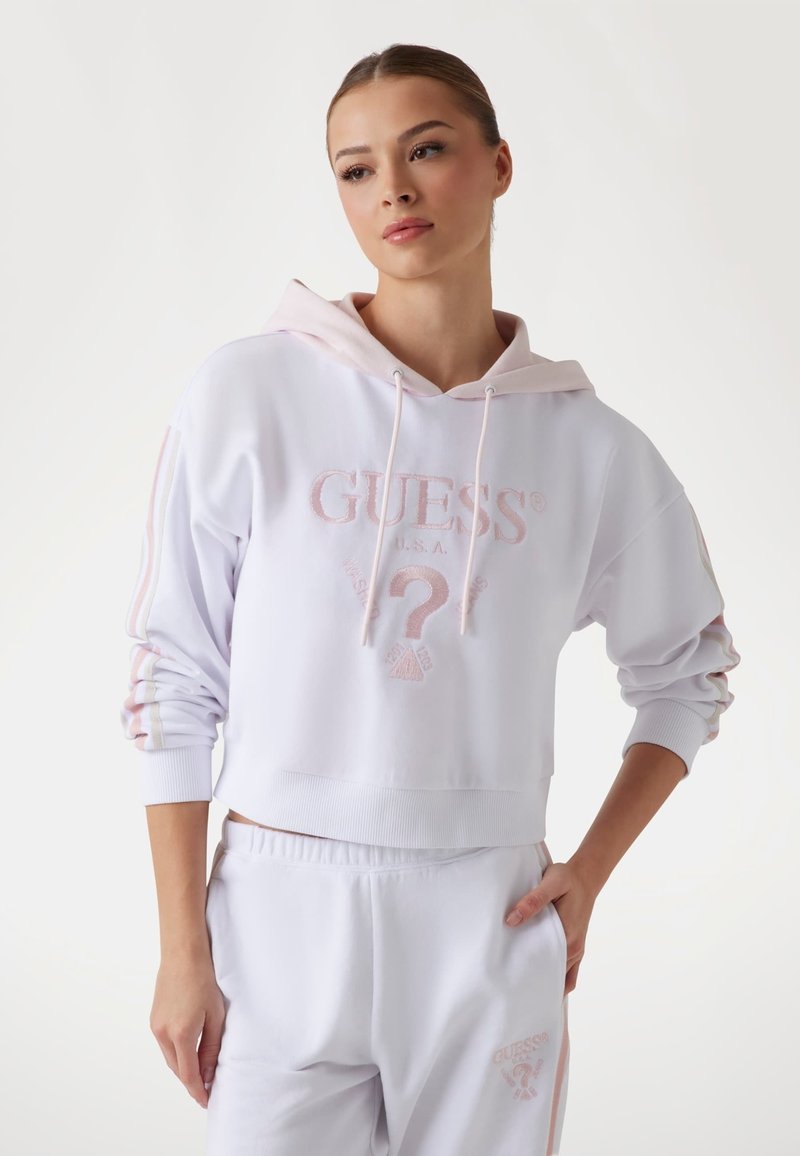 Witte cropped hoodie met roze accenten en geborduurd logo, voorzien van een capuchon met trekkoord en aansluitende manchetten, gecombineerd met bijpassende broeken.