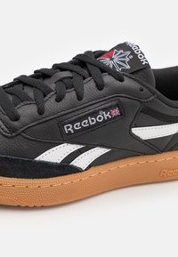 Svart lädersneaker med vita ränder, mockadetaljer och sula av gummigummi. Har Reebok-logotypen på tungan och sidan. Skosnörning.