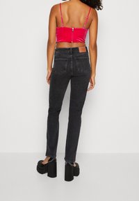 Jeans neri aderenti con un classico design a 5 tasche, abbinati a un top corto fucsia brillante con zip sul retro e spalline regolabili.