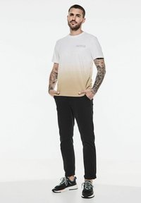 Vit och beige gradient t-shirt med korta ärmar, kompletterad med svarta byxor och svarta sneakers med vita accenter.