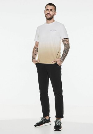 White and beige gradient t-shirt with short sleeves, complemented by black pants and black sneakers with white accents.