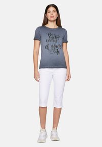 Grey cotton t-shirt with short sleeves and a round neckline, featuring black handwritten text. Paired with white cropped pants and sneakers.