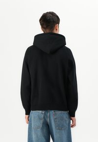 Black hoodie with a structured hood, ribbed cuffs, and hem. Paired with light blue denim jeans featuring back pockets. Simple and casual design.