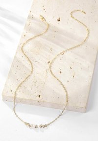 Goldkette mit einem zentralen Design, das aus drei Perlen und fünf sternförmigen Akzenten besteht. Vor einem strukturierten, neutralen Hintergrund.