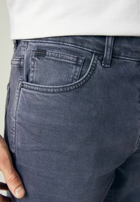 Jean en denim gris avec une texture lisse, présentant une étiquette en patch sur la poche arrière et le classique design à 5 poches.