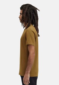 T-shirt a maniche corte, collo rotondo, di colore senape terroso, realizzato in cotone, con una vestibilità regolare e una texture liscia, senza motivi visibili.