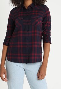 Marineblauwe en rode geruite flanellen overhemd met lange mouwen, opgerolde manchetten, twee borstzakken en knoopsluiting, gemaakt van zachte, gestructureerde stof.