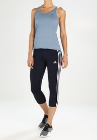 Ljusblå tops med rund halsringning och logotyp; mörkblå trekvarts leggings med vita sidostråkar; grå sportskor.