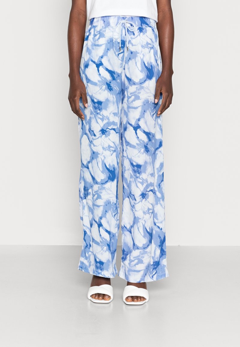 Pantalones sueltos de mármol azul y blanco con cinturilla elástica y cordón. La tela es ligera y fluye libremente. Combinados con zapatos blancos.