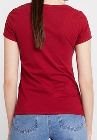 Red short-sleeve cotton t-shirt with a round neck, smooth texture, and fitted design, paired with high-waisted blue denim jeans.
